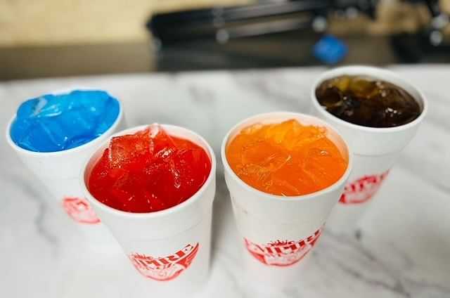 Four cups with colored ice cubes on a counter.