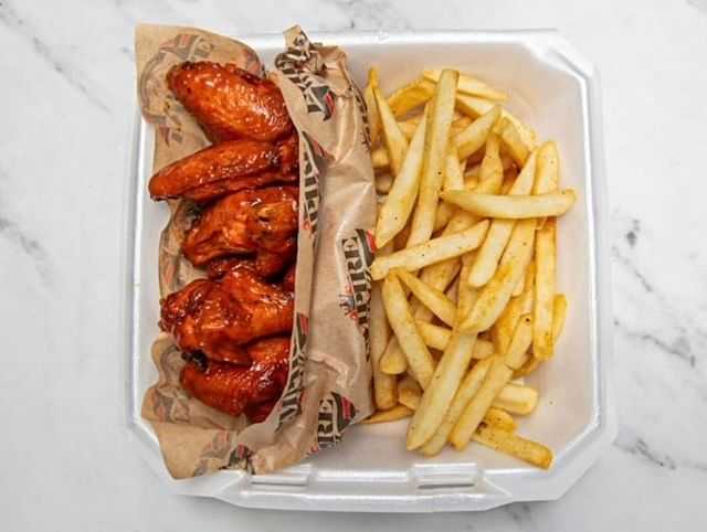 Buffalo wings and fries in a takeout container.